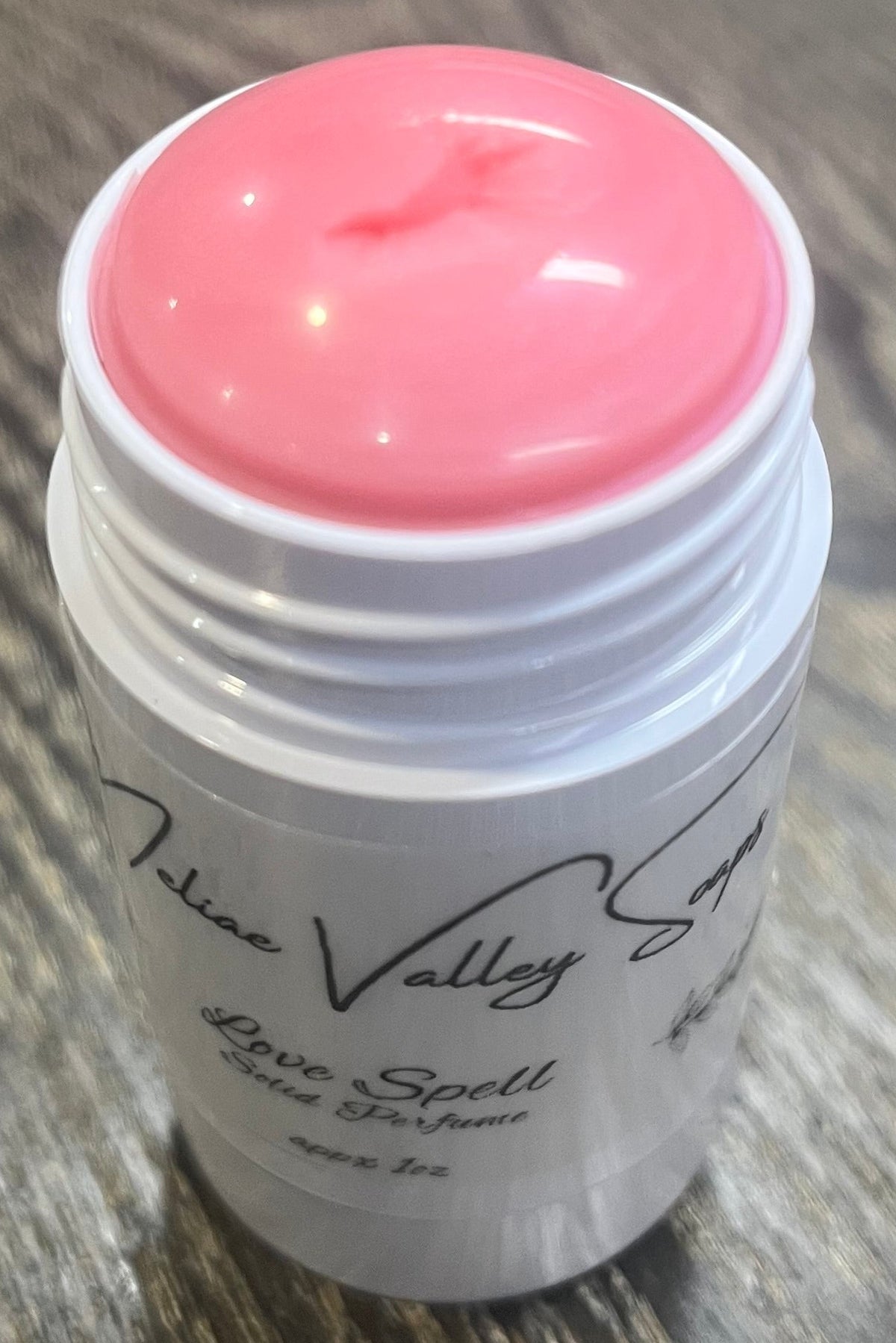 A white tube with a label on the front. The tube it open to show a pink balm. 